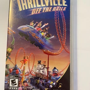 Puede incluir: Una caja de juego de PlayStation Portable (PSP) para el juego "Thrillville: Off the Rails". La caja es azul y presenta una imagen colorida de una montaña rusa con personas que la montan. El juego está clasificado como "E" para todos por la ESRB.