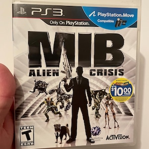 Könnte beinhalten: Ein Videospiel-Etui für die PlayStation 3-Konsole mit dem Spiel Men in Black: Alien Crisis. Das Etui ist weiß mit einem schwarzen und silbernen Design. Das Spiel zeigt einen Mann im schwarzen Anzug, der eine Waffe hält, und verschiedene außerirdische Kreaturen. Der Text auf dem Etui lautet "MIB Alien Crisis" und "PlayStation Move kompatibel".