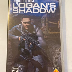 May include: A blue and white PlayStation Portable game case with the title "Syphon Filter: Logan's Shadow" and a picture of a man holding a rifle. The game is rated T for Teen by the ESRB.
