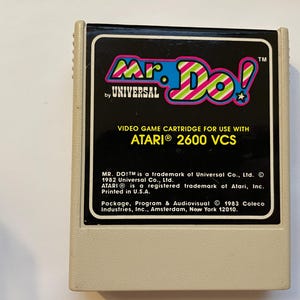 Peut inclure: Une cartouche de jeu vidéo vintage Mr. Do! pour l'Atari 2600 VCS. L'étiquette présente le logo du jeu aux couleurs vives et le texte "Mr. Do! by Universal". La cartouche est beige et rectangulaire.