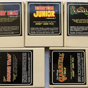 Peut inclure: Cinq cartouches de jeux vidéo Atari 2600 vintage. Les titres incluent "Donkey Kong", "Donkey Kong Junior", "Venture", "Mouse Trap" et "Carnival". Chaque cartouche a une étiquette noire avec le titre du jeu et la marque.