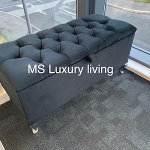 May include: Black velvet storage ottoman with a tufted top and silver legs. The ottoman has a hinged lid and is labelled "MS Luxury living".
