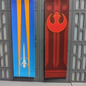 May include: Two rectangular banners. One is blue with orange stripes and a white and silver emblem. The other is red with a red emblem and vertical stripes. The banners are displayed against a gray wall.