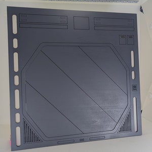 May include: A dark gray, rectangular panel with a large, octagonal cutout in the center. The panel has a series of rectangular cutouts along the top and sides, and a series of smaller, rectangular cutouts along the bottom. The panel has the number "000" printed on the bottom.