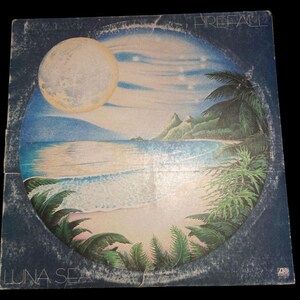 May include: A blue vinyl record album cover with a circular image of a beach scene with a full moon, palm trees, and a small island. The album title is "Luna Sea" and the band name is "Firefall".