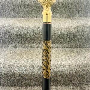 May include: A black walking stick with an ornate gold-coloured handle and a decorative floral design.