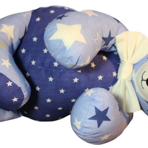 May include: A plush teddy bear in shades of blue, adorned with white stars. The bear features a cream-colored bow and black button eyes. The bear's body is a patchwork of different blue fabrics.