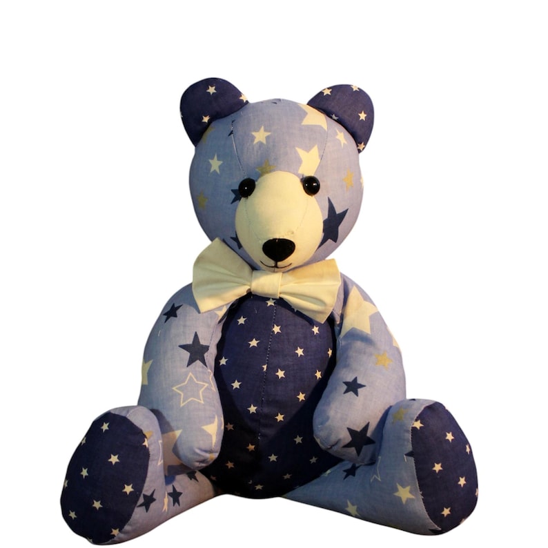May include: A handmade teddy bear with a blue and white star pattern. The bear has a cream-colored bow tie and a cream-colored face. The bear is sitting with its legs outstretched. The bear's ears and paws are a darker blue color.
