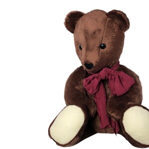 May include: A brown teddy bear with a burgundy scarf. The bear has dark eyes, a black nose, and cream-coloured paws. The plush toy is sitting upright, with its arms and legs extended.