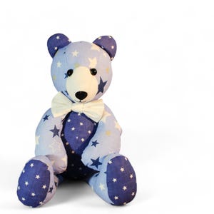 May include: A plush teddy bear with a blue and white star pattern. The bear has a cream-colored bow tie and a light blue body with dark blue accents. The bear is sitting upright.