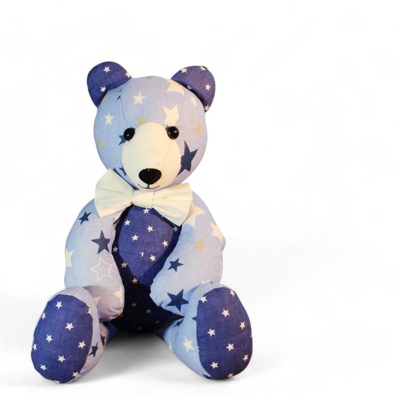 May include: A plush teddy bear with a blue and white star pattern. The bear has a cream-colored bow tie and a light blue body with dark blue accents. The bear is sitting upright.