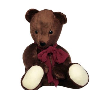 May include: A brown teddy bear with a dark red scarf. The bear has dark eyes and light patches on its feet. The plush toy is sitting down. The bear is made of soft, plush material. The scarf is tied in a bow. The bear is a classic toy.
