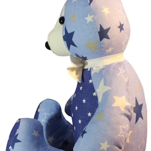 May include: A handmade teddy bear with a light blue and navy star pattern. The bear has a white muzzle, a cream-colored bow, and black eyes. The bear is a soft toy.