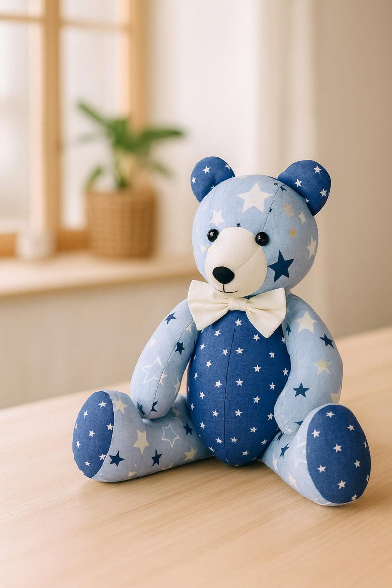 May include: A plush teddy bear with a light blue and navy blue star pattern. The bear has a white muzzle and a cream-colored bow tie. The bear is sitting on a wooden surface.