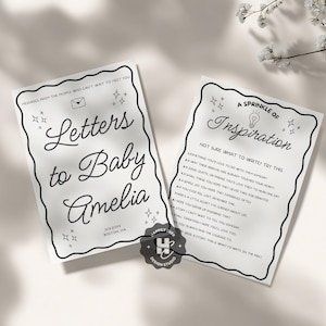 May include: Two white cards with black text and decorative borders. One card reads "Letters to Baby Amelia" with a date and location. The other card says "A Sprinkle of Inspiration" with writing prompts. The cards are from Happily Ever Design Studio.