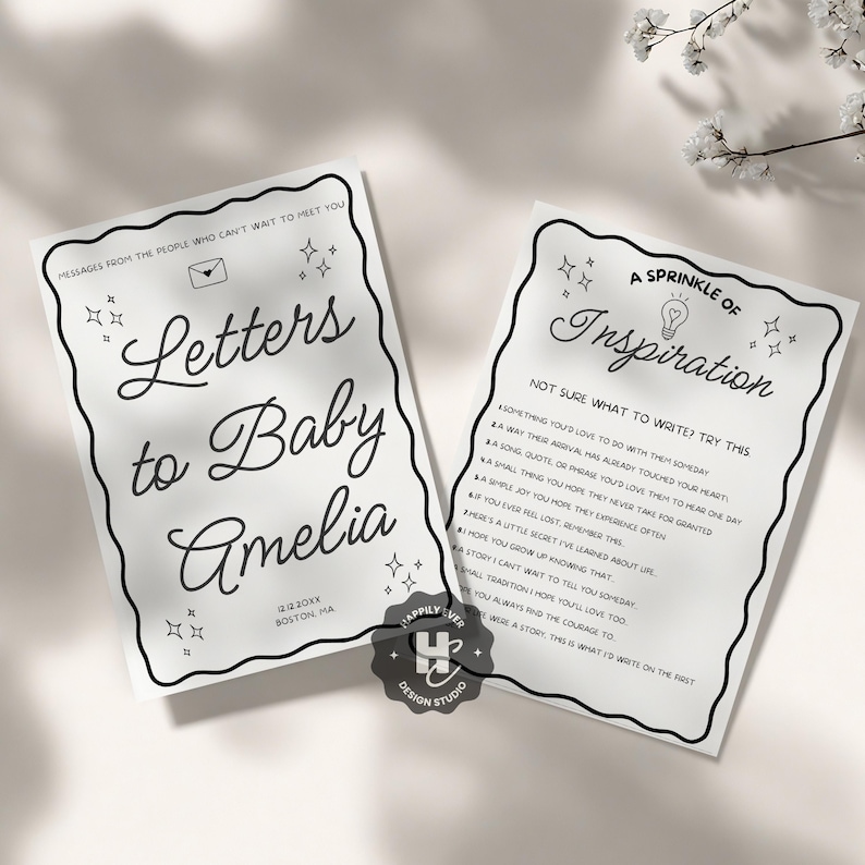 May include: Two white cards with black text and decorative borders. One card reads "Letters to Baby Amelia" with a date and location. The other card says "A Sprinkle of Inspiration" with writing prompts. The cards are from Happily Ever Design Studio.