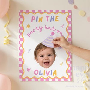 May include: A rectangular party game poster with a pink and white checkered border. The text reads PIN THE party hat on OLIVIA. A cutout of a smiling child's face is centered on the white background, with a hand placing a purple striped party hat.