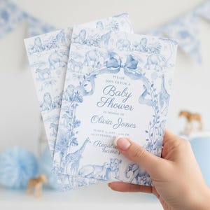 Può includere: Inviti per baby shower con un design di animali safari blu e bianco. Gli inviti presentano un fiocco e un bordo floreale, con il testo "Unisciti a noi per un Baby Shower in onore di Olivia Jones."