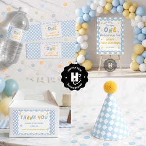 May include: A collection of party supplies for a first birthday celebration. Includes water bottle labels, a welcome sign, a party favor box, and a checkered party hat. The theme is blue and white with yellow accents. The sign reads "It's fun to be ONE."