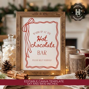 May include: A framed sign with the text "Warm up at the Hot Chocolate Bar" in red script. The wooden frame has decorative carvings. The sign is surrounded by mugs, marshmallows, cinnamon sticks, and pine cones, creating a cozy, festive atmosphere.