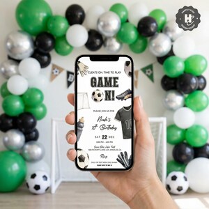 May include: A smartphone displays a soccer-themed birthday invitation with the text "Game On!" and details for Noah's 10th birthday. The background features a balloon arch in green, black, white, and silver, with soccer balls.