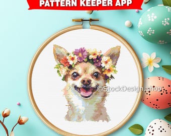 May include: Cross stitch pattern of a chihuahua wearing a flower crown. The pattern is in a white hoop with a wooden frame. The chihuahua is looking at the viewer with a happy expression.