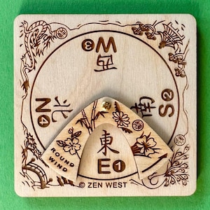 May include: A wooden compass with engraved Asian-inspired designs and text. The compass features a rotating pointer and a circular dial with directional markings. The text includes "ROUND WIND" and "ZEN WEST".