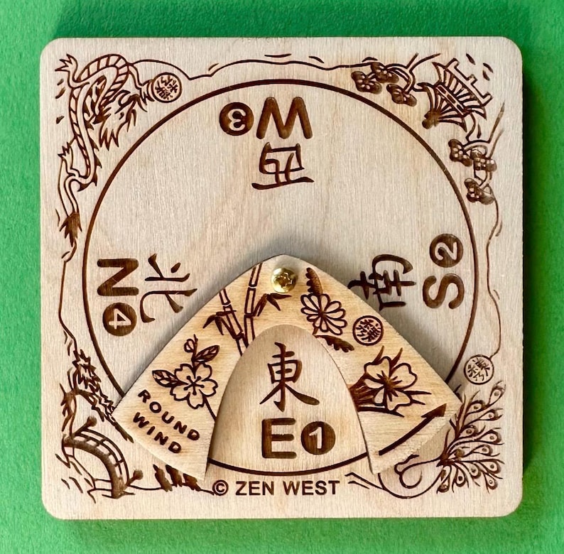 Peut inclure: Une boussole en bois avec des motifs et du texte grav&eacute;s d'inspiration asiatique. La boussole comporte un pointeur rotatif et un cadran circulaire avec des indications directionnelles. Le texte comprend "ROUND WIND" et "ZEN WEST".