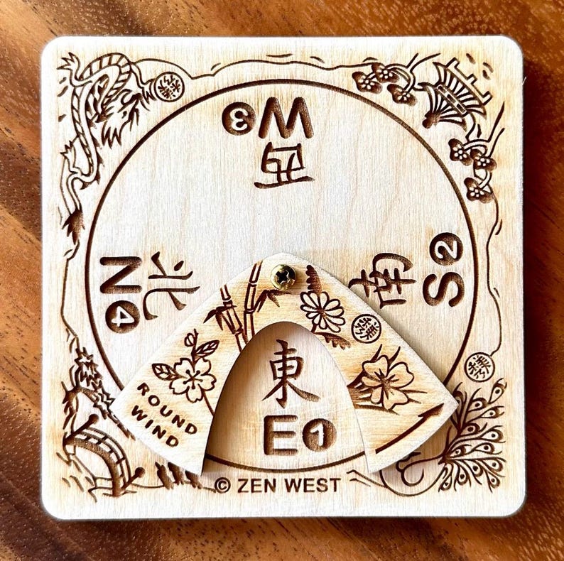 Peut inclure: Une boussole carr&eacute;e en bois avec des motifs et du texte grav&eacute;s d'inspiration asiatique. La boussole comporte un pointeur rotatif et est &eacute;tiquet&eacute;e avec les points cardinaux et le texte "ROUND WIND" et "ZEN WEST".