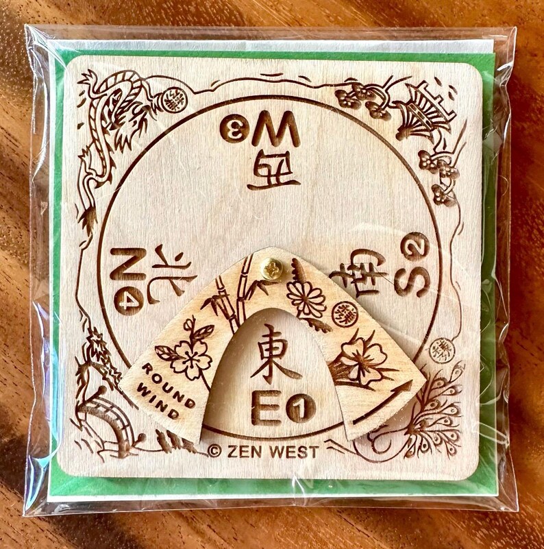 Peut inclure: Une boussole en bois avec un pointeur rotatif, avec des caract&egrave;res chinois grav&eacute;s et des motifs floraux. La boussole est &eacute;tiquet&eacute;e avec "ROUND WIND" et "ZEN WEST". Elle est emball&eacute;e dans une pochette en plastique transparent.