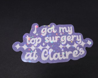 May include: A purple iridescent sticker with the text "I got my top surgery at Claire's" in white lettering.
