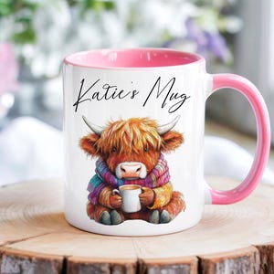 Può includere: Tazza in ceramica bianca con interno e manico rosa, con un'illustrazione ad acquerello di una mucca delle Highlands con una sciarpa e una tazza. La tazza è scritta "Katie's Mug".