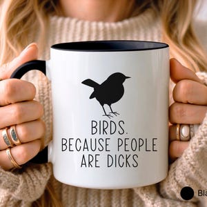 Pode incluir: Caneca de cer&acirc;mica branca com interior e al&ccedil;a pretos. A caneca apresenta uma silhueta preta de um p&aacute;ssaro e o texto "BIRDS. BECAUSE PEOPLE ARE DICKS" em letras pretas. A caneca &eacute; segurada por uma pessoa.