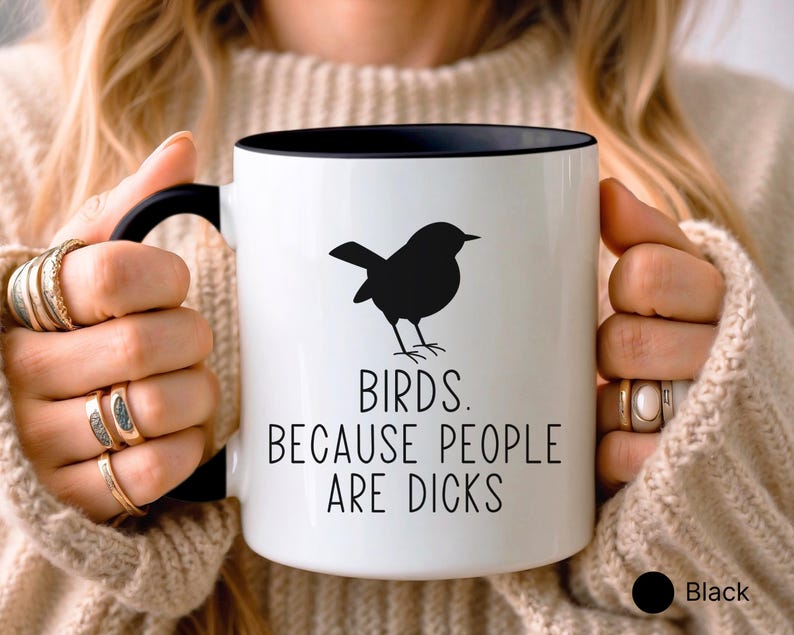 Pode incluir: Caneca de cer&acirc;mica branca com interior e al&ccedil;a pretos. A caneca apresenta uma silhueta preta de um p&aacute;ssaro e o texto "BIRDS. BECAUSE PEOPLE ARE DICKS" em letras pretas. A caneca &eacute; segurada por uma pessoa.