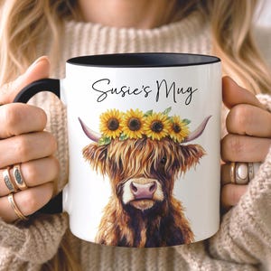 May include: White ceramic mug with a black handle and rim, featuring a watercolor illustration of a Highland cow wearing a sunflower crown. The mug has the text "Susie's Mug" in a script font.