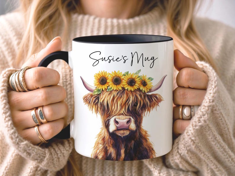 May include: White ceramic mug with a black handle and rim, featuring a watercolor illustration of a Highland cow wearing a sunflower crown. The mug has the text "Susie's Mug" in a script font.
