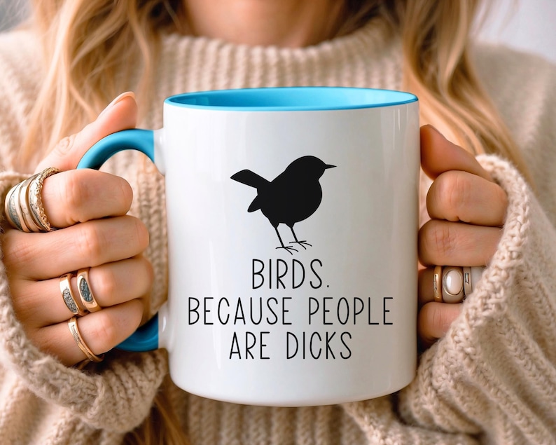 Pode incluir: Caneca de cer&acirc;mica branca com interior e al&ccedil;a azuis. A caneca apresenta uma silhueta preta de um p&aacute;ssaro e o texto "BIRDS. BECAUSE PEOPLE ARE DICKS" em preto, centrado na frente.