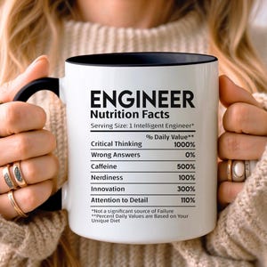 May include: White ceramic mug with a black rim and handle. The mug features a black and white graphic that reads "Engineer Nutrition Facts" with a list of "Nutrition Facts" for an engineer, including critical thinking, wrong answers, caffeine, nerdiness, innovation, and attention to detail.