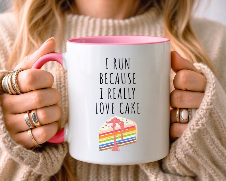 May include: White ceramic mug with a pink rim and handle. The mug has a black text that reads "I run because I really love cake" and a colorful cake illustration.