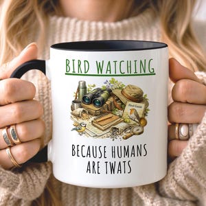 May include: A white ceramic mug with a black handle and the text "But First, Coffee" in a black, handwritten-style font. The mug is on a white surface.