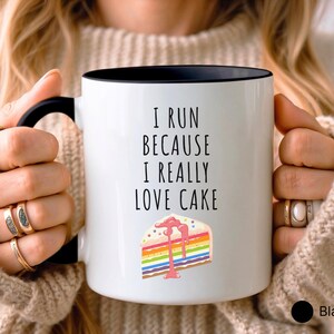 May include: White coffee mug with a black rim and handle. The mug has the text "I run because I really love cake" and a colorful cake slice with pink frosting.