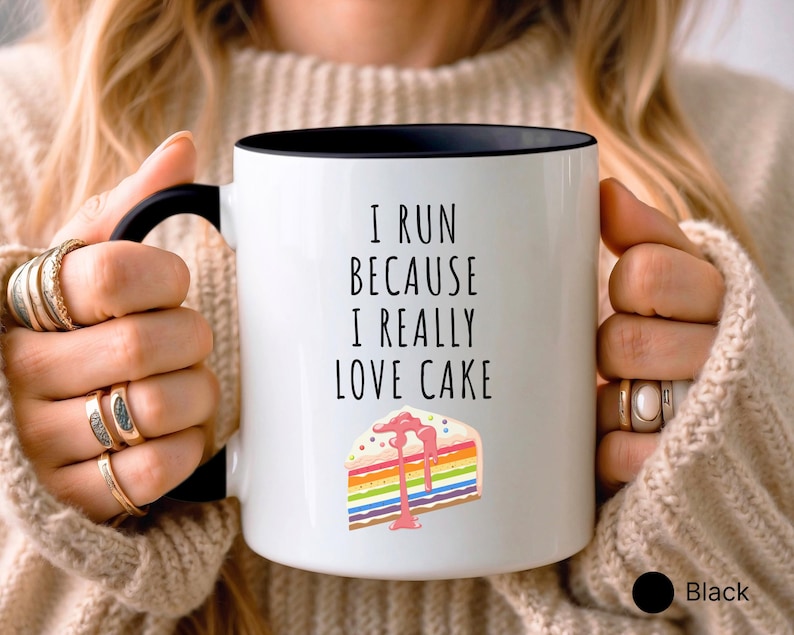 May include: White coffee mug with a black rim and handle. The mug has the text "I run because I really love cake" and a colorful cake slice with pink frosting.