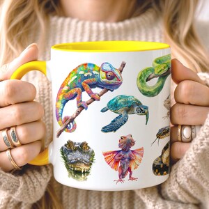 Könnte beinhalten: Ein weißer Keramikbecher mit einem leuchtend gelben Henkel und Innenrand, der mit einer farbenfrohen Illustration verschiedener Reptilien und Amphibien bedruckt ist, darunter ein buntes Chamäleon, eine Meeresschildkröte, ein Alligator und eine Kragenechse.