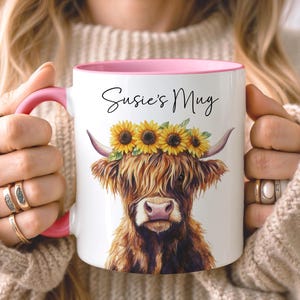 May include: White ceramic mug with a pink interior and handle, featuring a watercolor illustration of a Highland cow wearing a sunflower crown. The mug has the text "Susie's Mug" in black script.