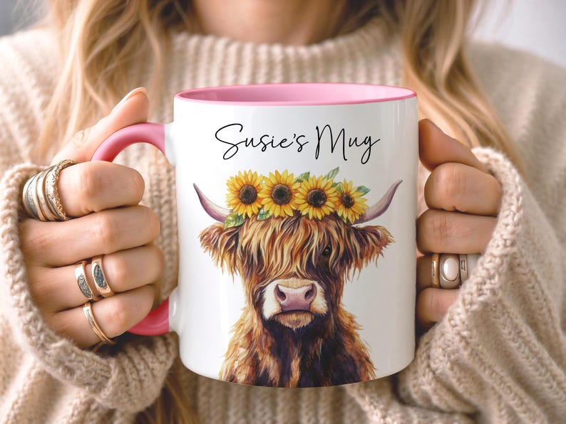 May include: White ceramic mug with a pink interior and handle, featuring a watercolor illustration of a Highland cow wearing a sunflower crown. The mug has the text "Susie's Mug" in black script.