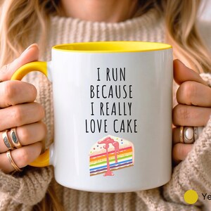 May include: White ceramic mug with a yellow rim. The mug has a black text that reads "I run because I really love cake" and a colorful cake illustration.