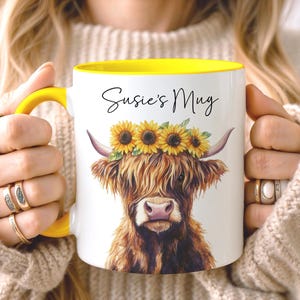 May include: White ceramic mug with a yellow interior and handle. The mug features a watercolor illustration of a Highland cow wearing a sunflower crown. The text "Susie's Mug" is written in black script.