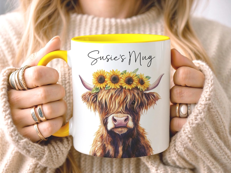May include: White ceramic mug with a yellow interior and handle. The mug features a watercolor illustration of a Highland cow wearing a sunflower crown. The text "Susie's Mug" is written in black script.
