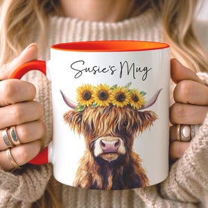 May include: White ceramic mug with a red handle and interior. The mug features a watercolor illustration of a Highland cow wearing a sunflower crown, with the text "Susie's Mug" in black script.
