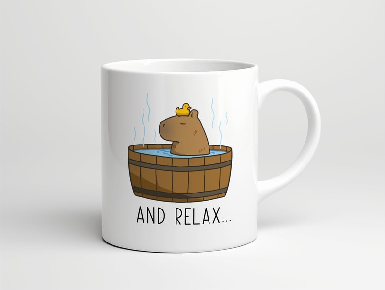 May include: White ceramic mug with a cartoon illustration of a capybara in a wooden hot tub with a yellow rubber ducky on its head. The text "AND RELAX..." is printed below the image.